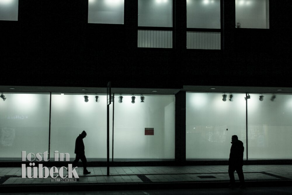 Mühlenstrasse Lübeck 2 Silhouetten vor leeren beleuchteten Schaufenstern